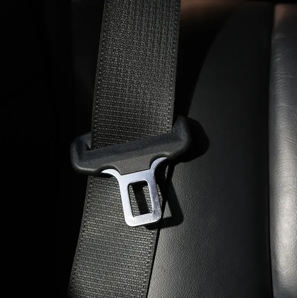 Close view of seatbelt webbing threaded through a moulded latch plate against a vehicle seat.