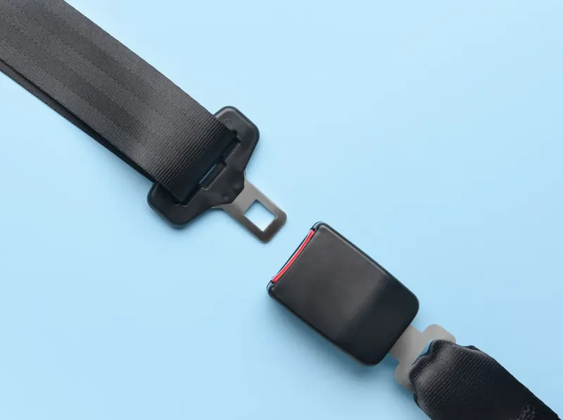 A seatbelt latch plate and a separate buckle section laid flat and apart on a plain light blue background.