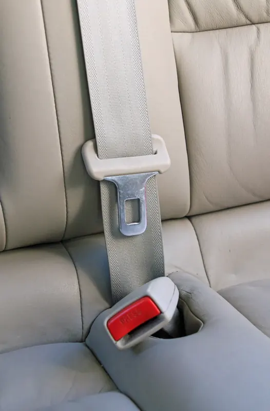 A light grey three-point seatbelt running diagonally across a pale leather rear seat into a red-release buckle.